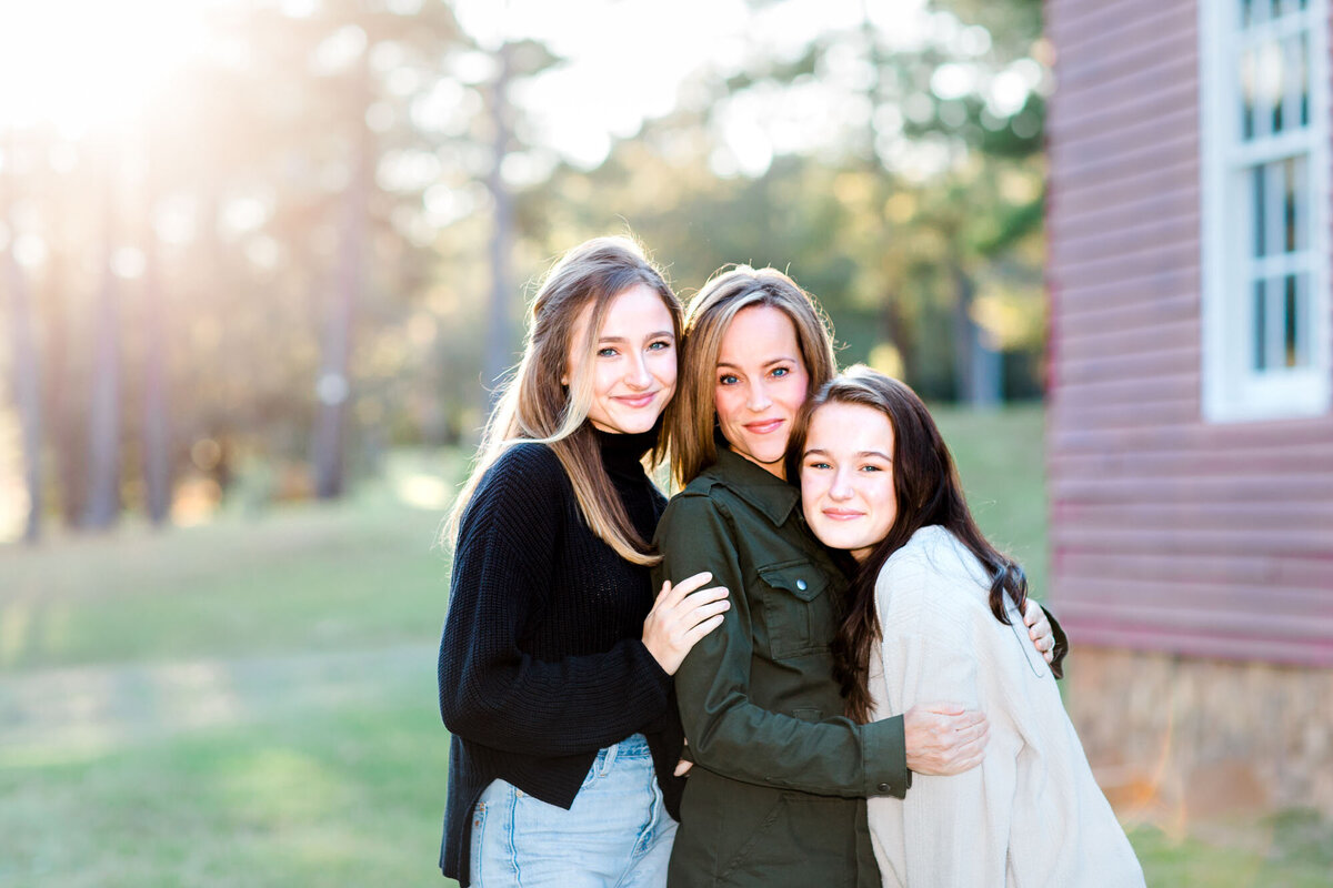 A mother and her two daughters hug in tight for their family portrait together as the sunlight filters in from behind.