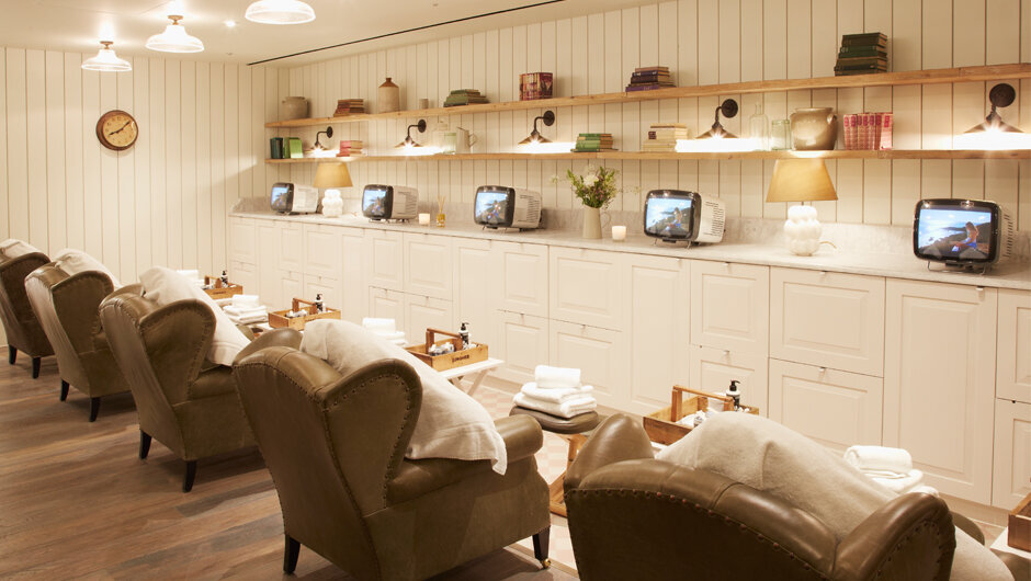 Nail Salon with vintage style wingback green leather chairs in front of white millwork,  retro TV's, and vintage shelves and objects