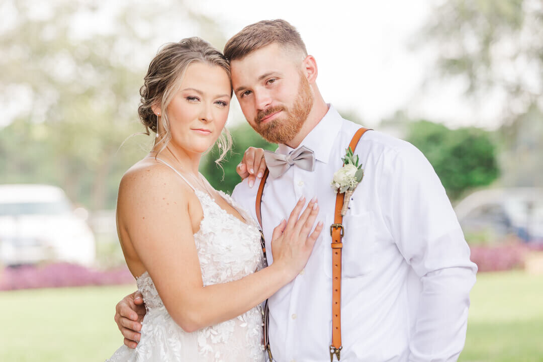 A couple snuggles in a lawn in a lace dress and white shirt with suspenders for an Arkansas wedding photographer