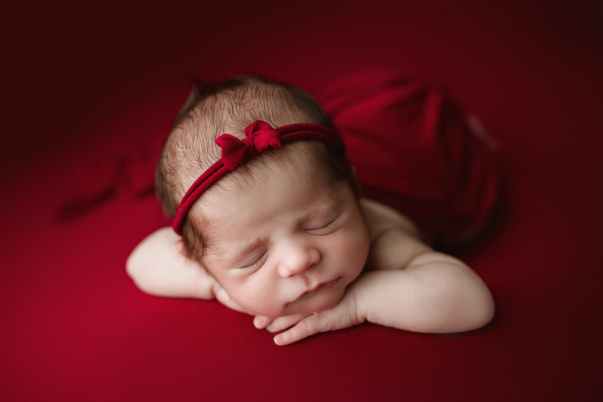 Baby girl posed on red with red headband.