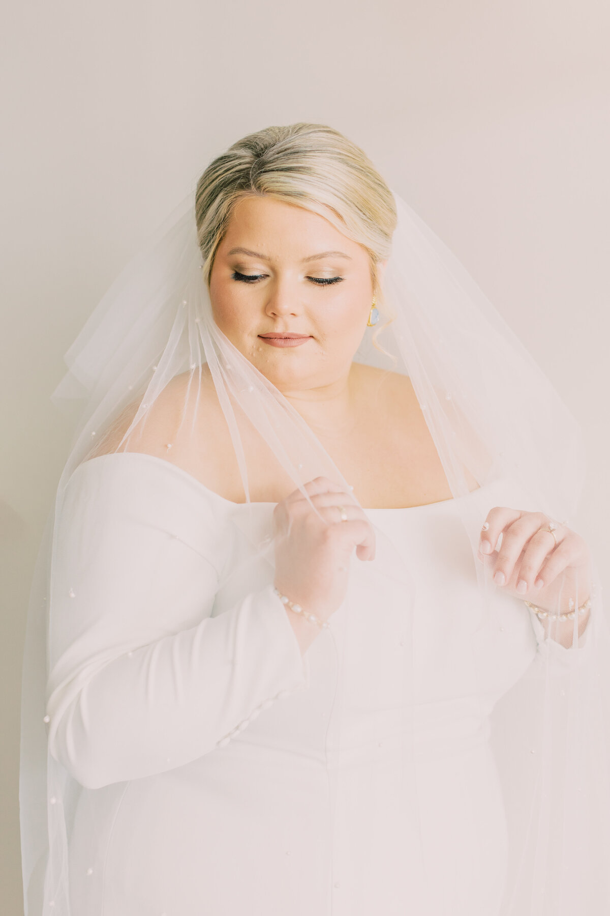 Bride with blonde hair holding veil in front of dress