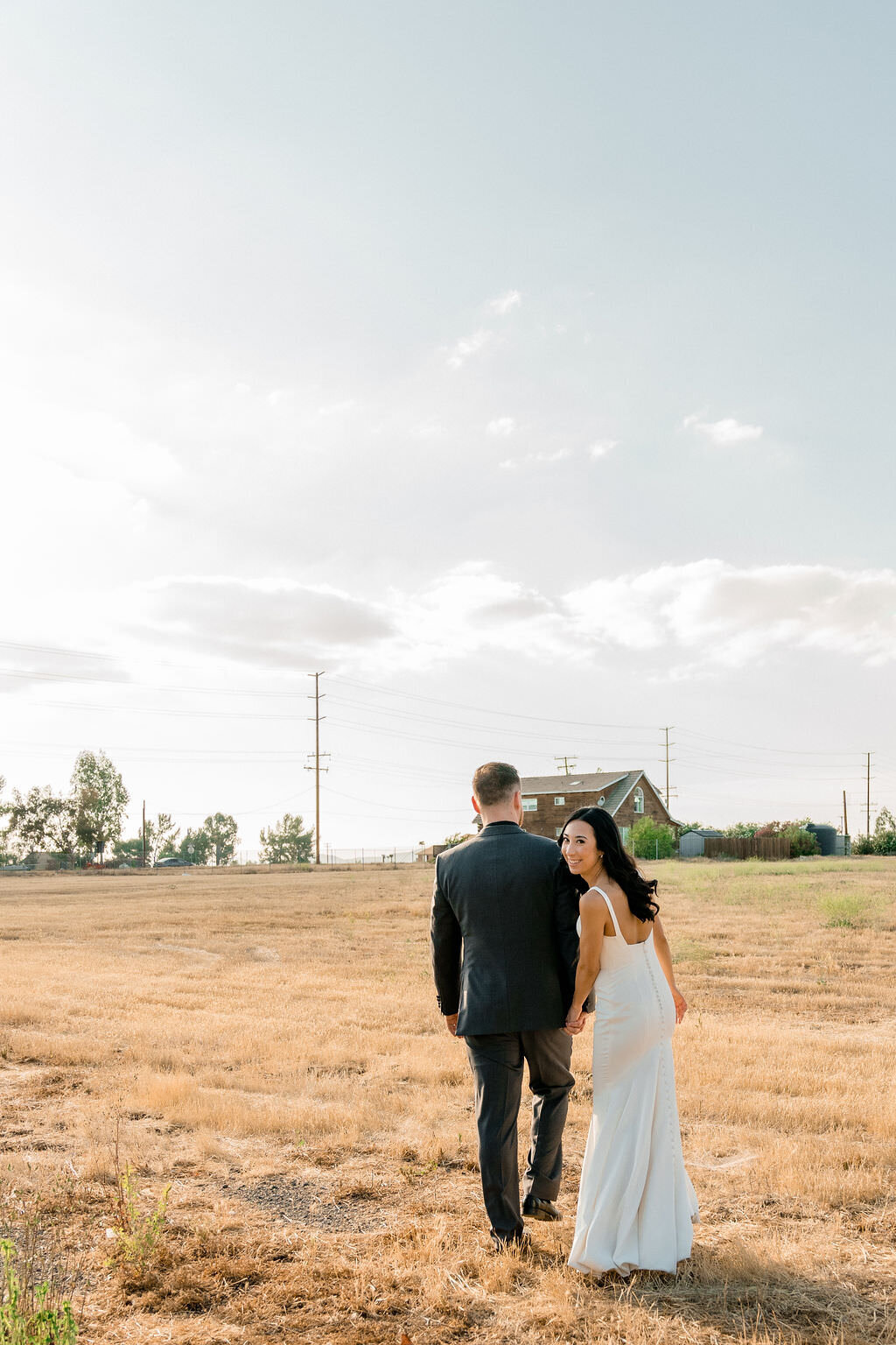 couple walking in a field as the bride looks back over her shoulder