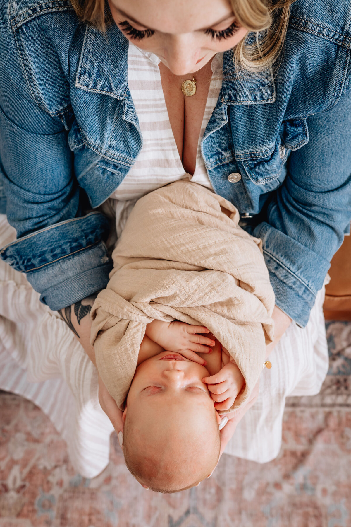 A close-up shot from above of a mother holding her swaddled newborn on her lap, with her hands cradling the baby gently.