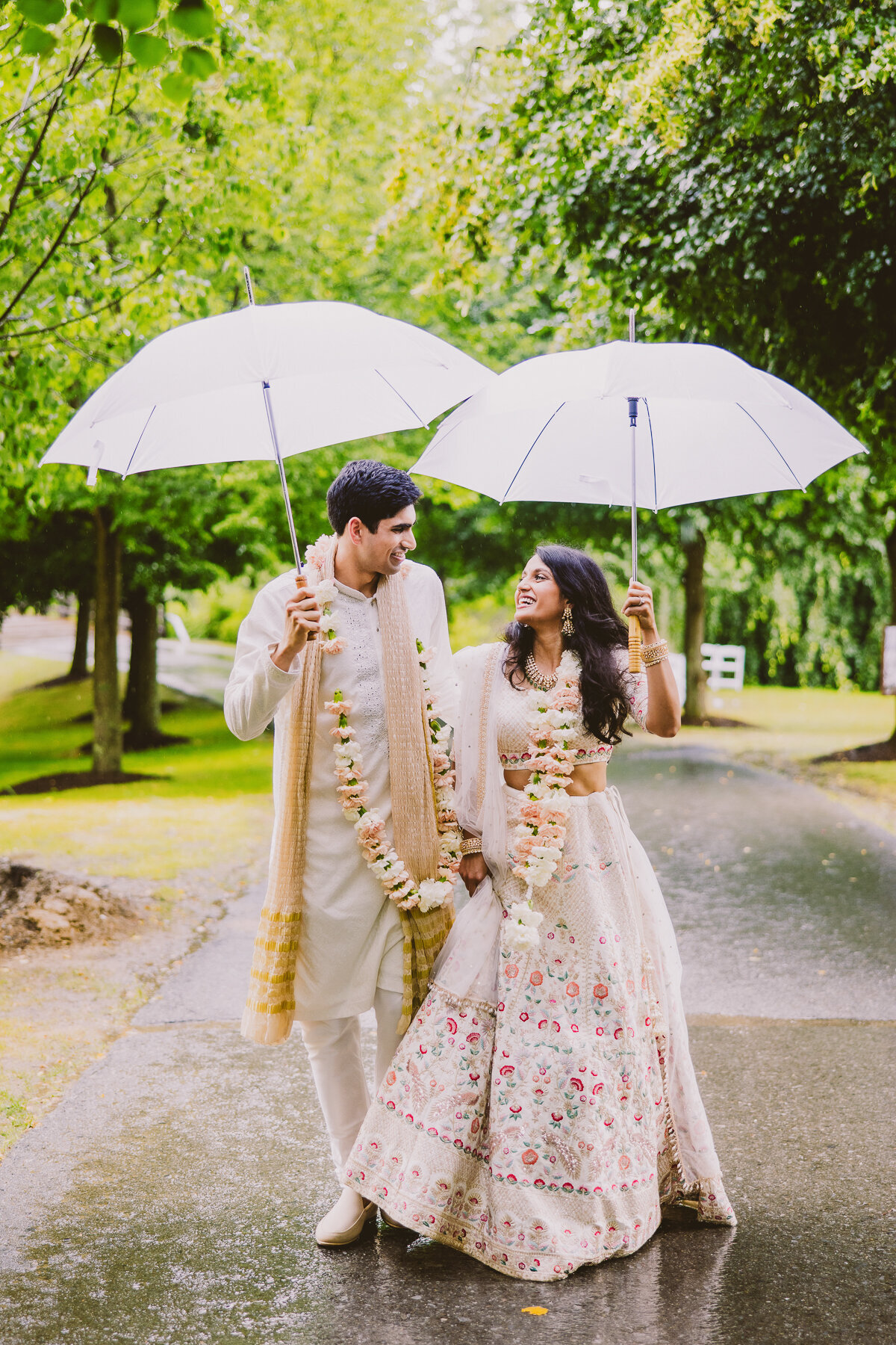 Indian bride and groom exiting from their hindu wedding ceremony walking away in the rain with umbrellas