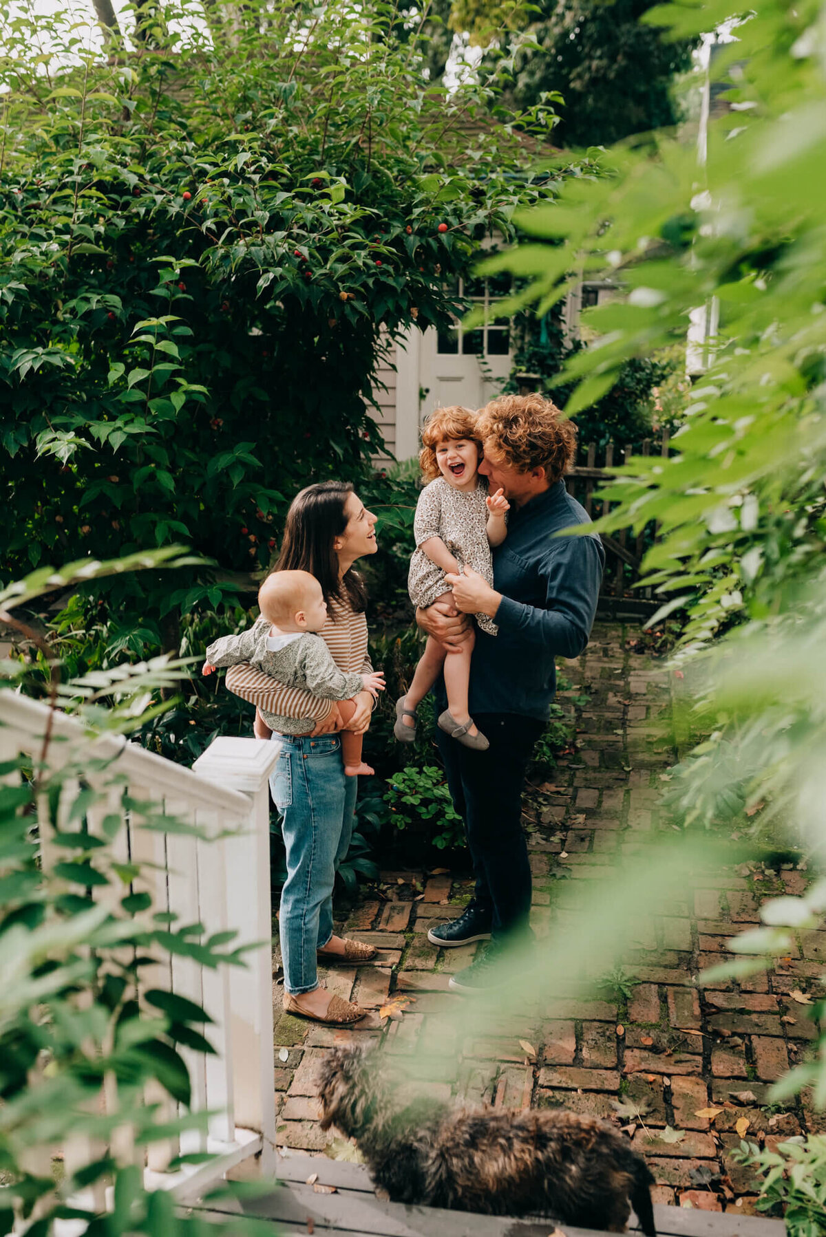 A mother and father stand together on their back deck, the mother holds their youngest daughter and the father holds the oldest daughter