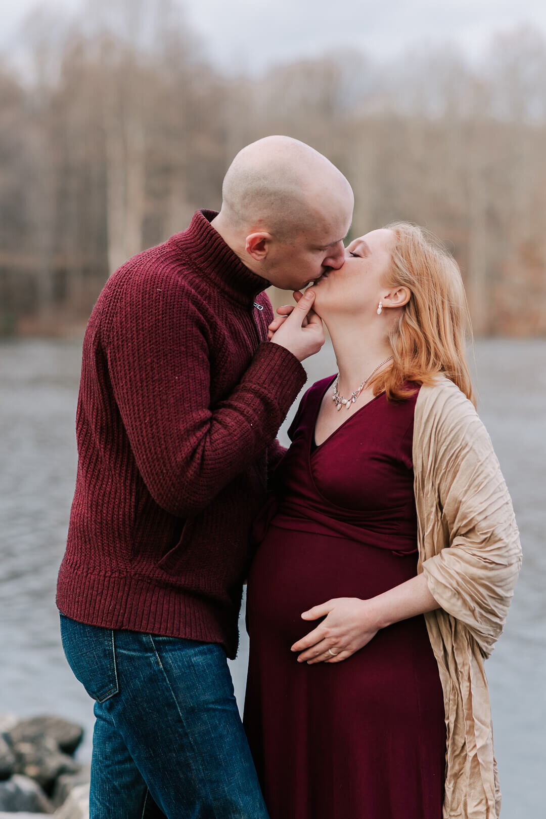 A man kisses his red-haired pregnant wife in front of Centennial Lake