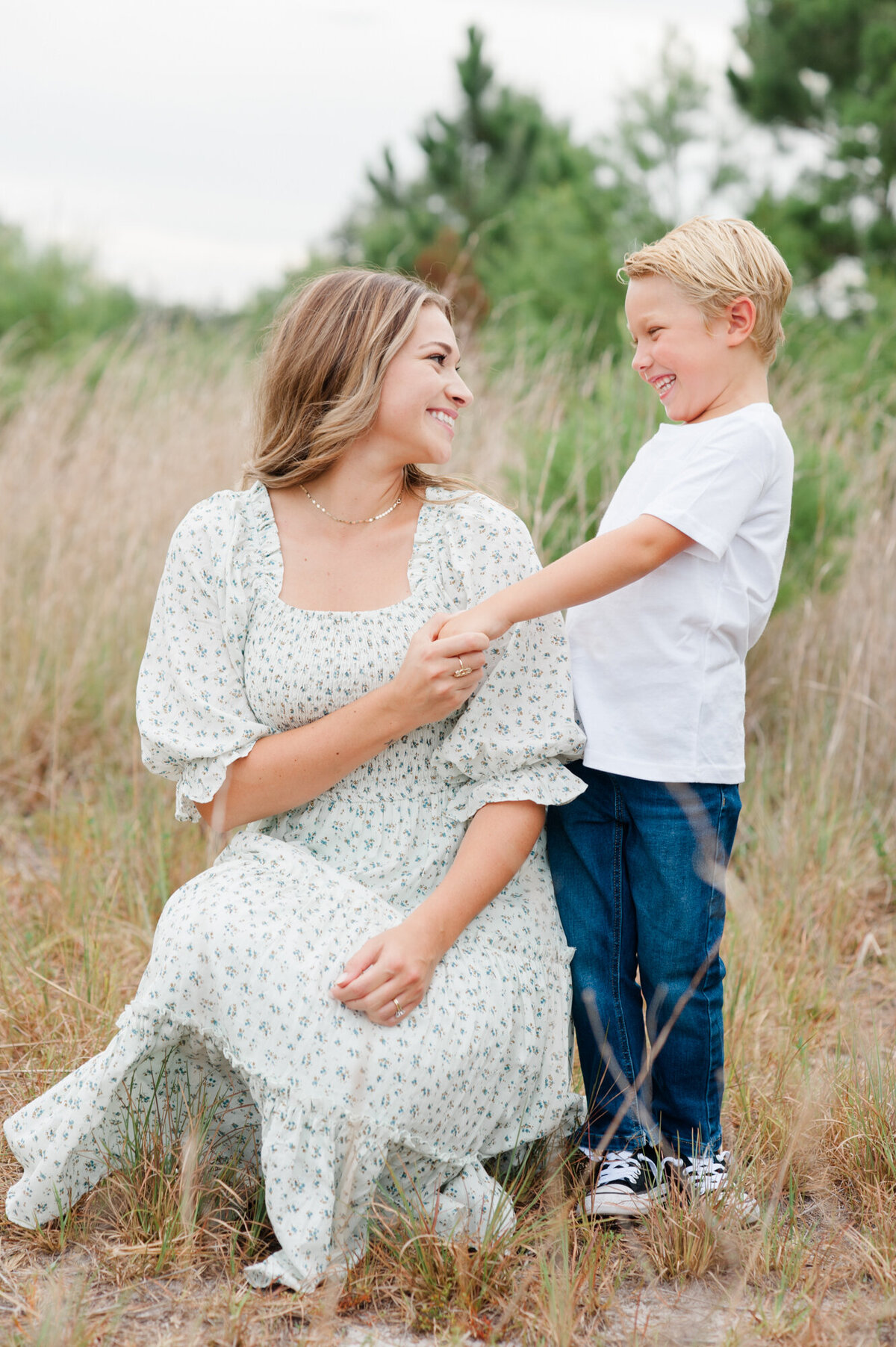 Mom and son holding hands and smiling at each other while standing in a tall grass field