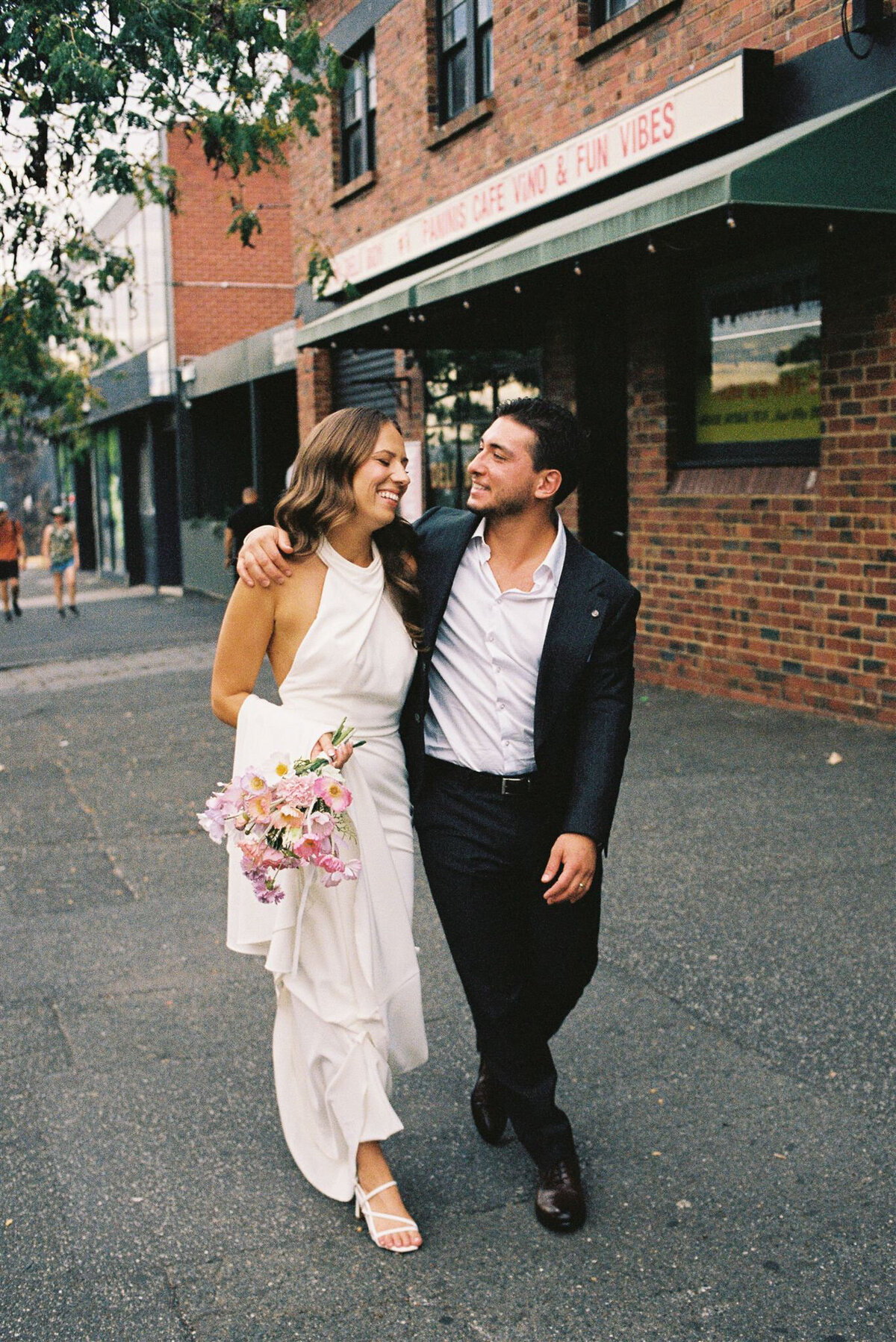 Newlyweds walking hand-in-hand through the streets of South Melbourne, enjoying a relaxed and candid moment on 35mm film.
