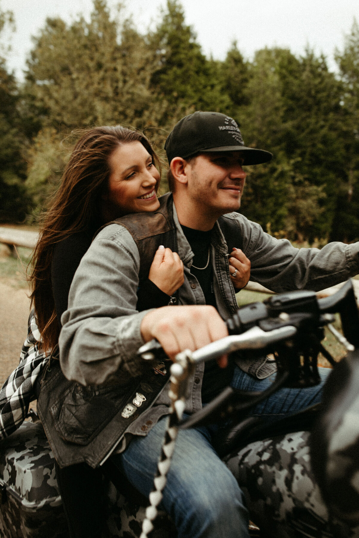 Girl holding onto guy wearing biker jacket as they ride a motorcycle down the road