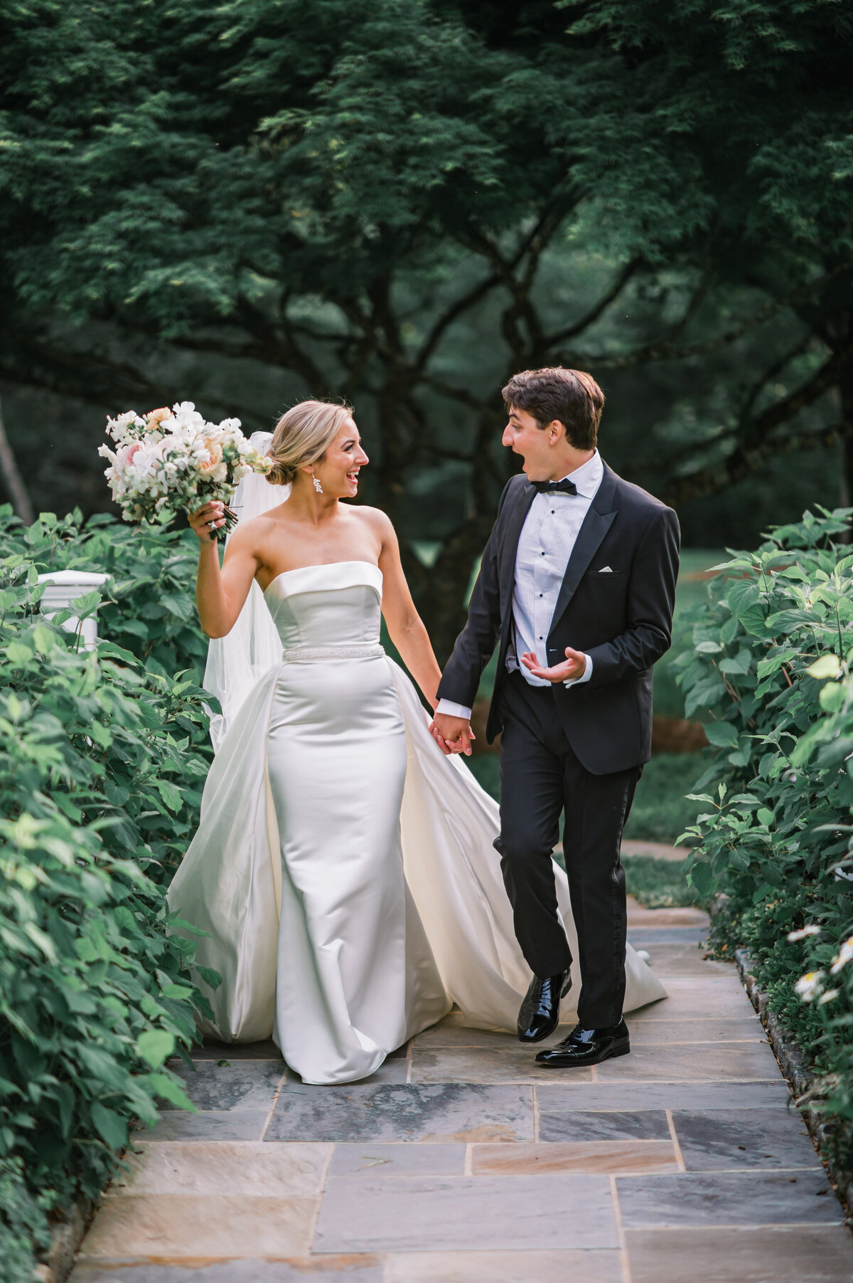 Joyful bride and groom walking hand in hand along a garden path at Old Edwards Inn in Highlands, North Carolina.