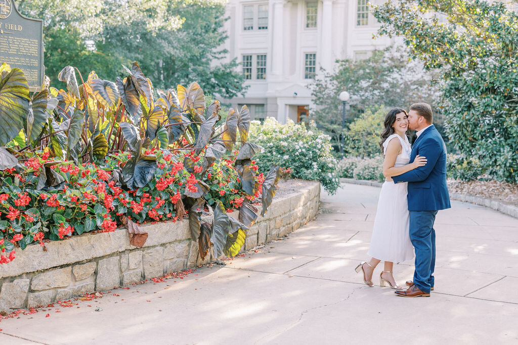 Man in blue suit kisses woman in white dress at Athens City Hall with banana leaf plants in background