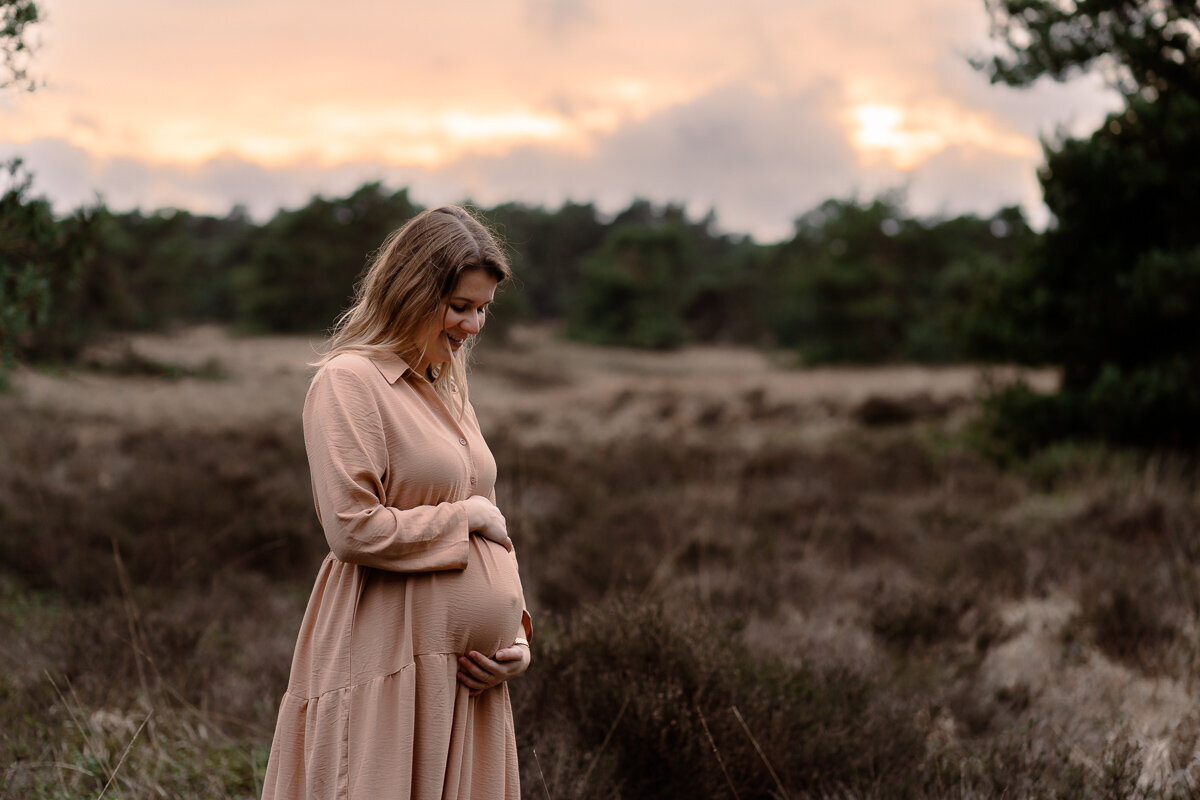 zwangere vrouw kijkt liefdevol en lachend naar haar groeiende buik tijdens een zwangerschapsshoot