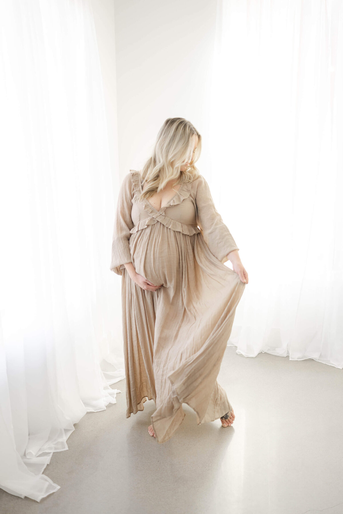 mom to be embracing her baby bump in a flowing dress from an oklahoma city maternity store