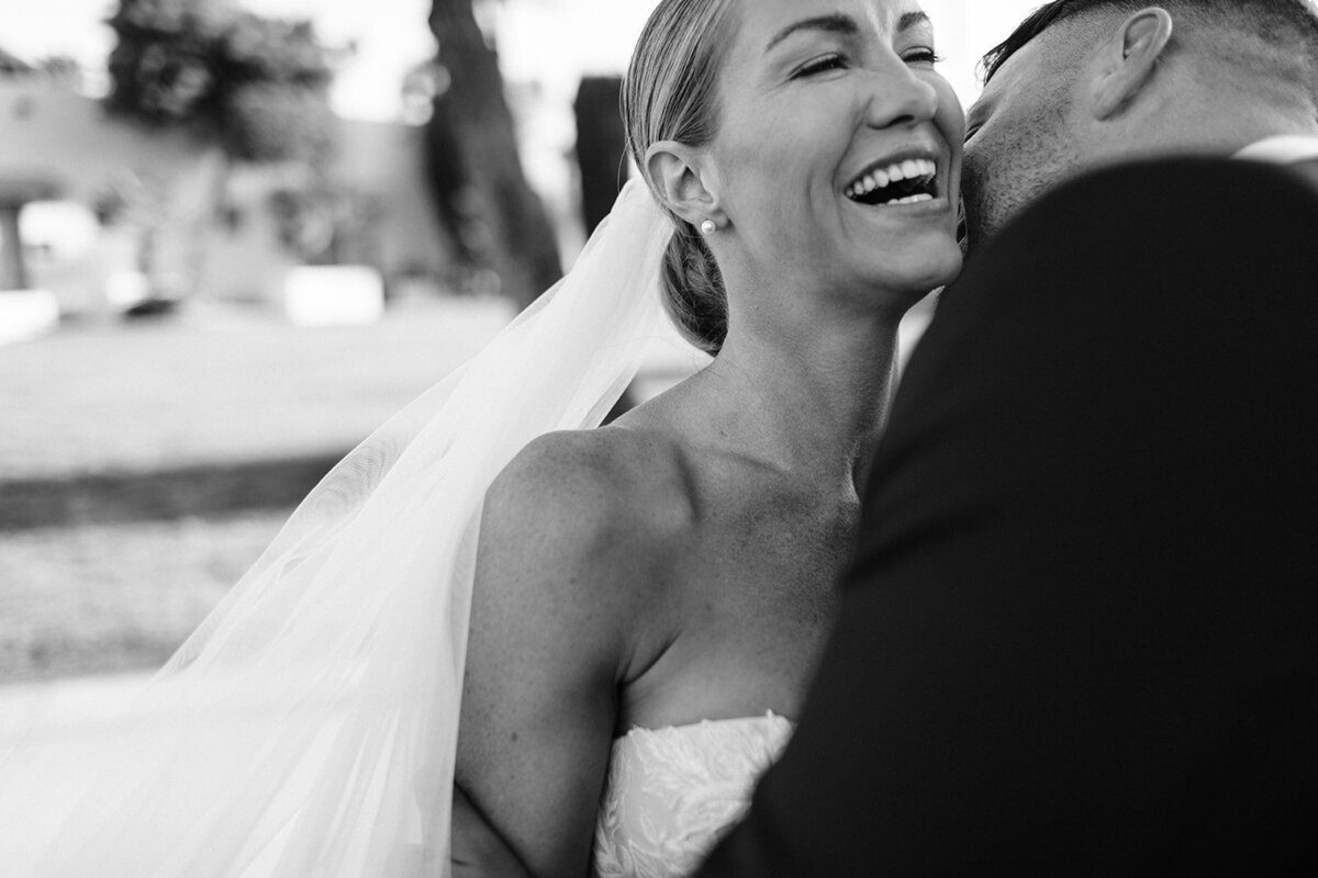 Bride laughing joyfully as the groom embraces her, outdoors on a sunny day. Captured by a talented Toronto wedding photographer, the image exudes timeless romance in black and white.