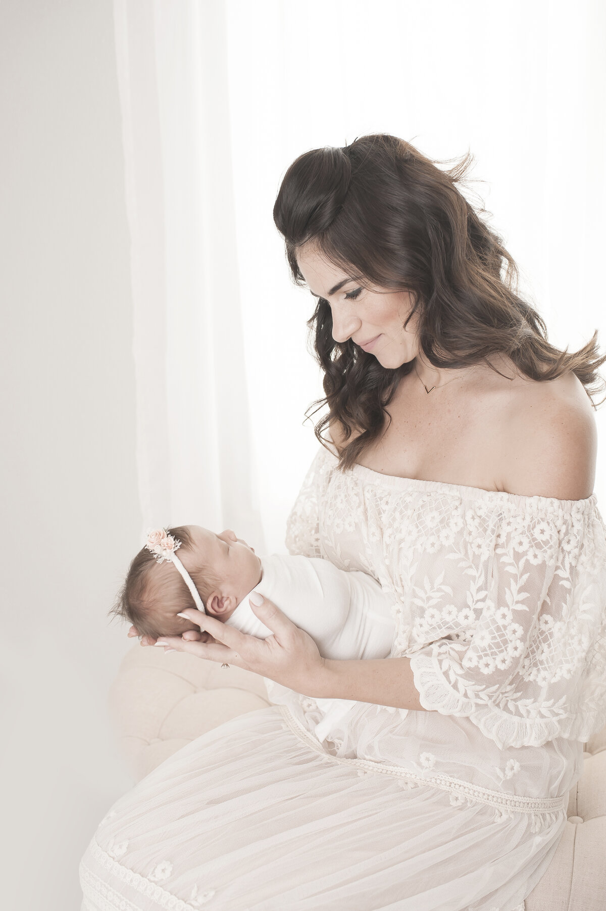 Woman in lace dress sitting and holding newborn baby girl