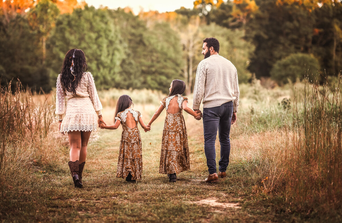 A family of four is holding hands and walking away from the camera.