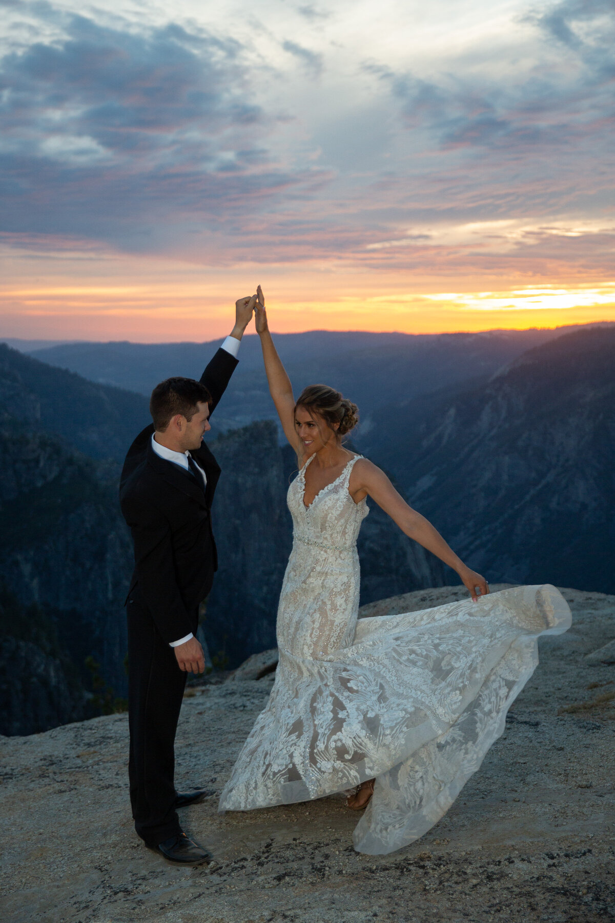 A groom twirls his bride as her dress swings out next to her and the sunsets behind them.