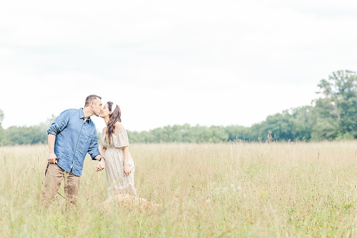 couple kiss in field during maternity photo session at heard farm in Wayland Massachusetts with Sara Sniderman Photography