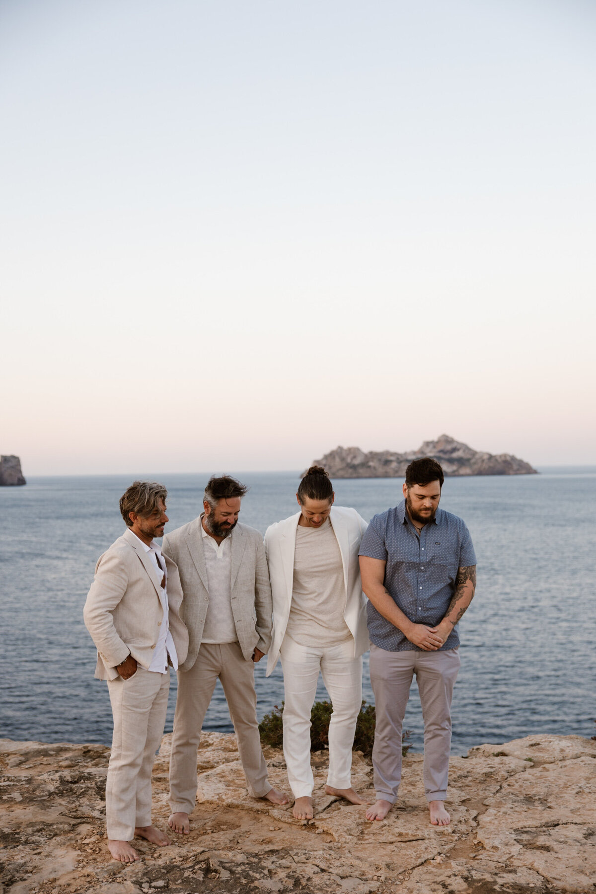 Four men looking at the ground and holding each other at an Ibiza wedding