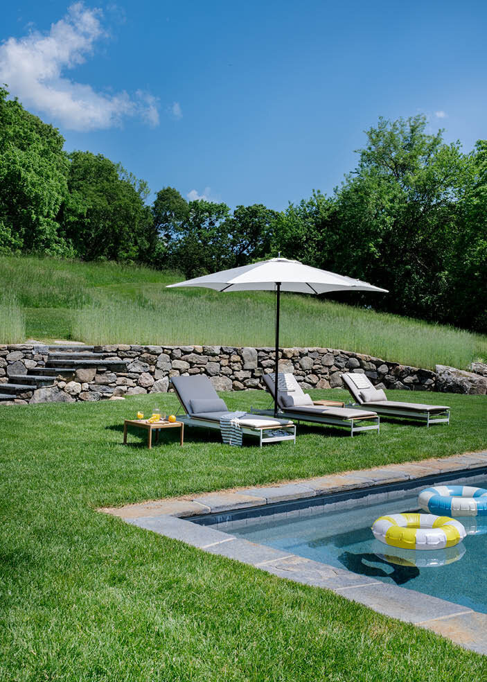 A different view of the Concord estate pool, showcasing modern chaise lounges from Design Within Reach and a Tucci umbrella, offering a luxurious outdoor experience.