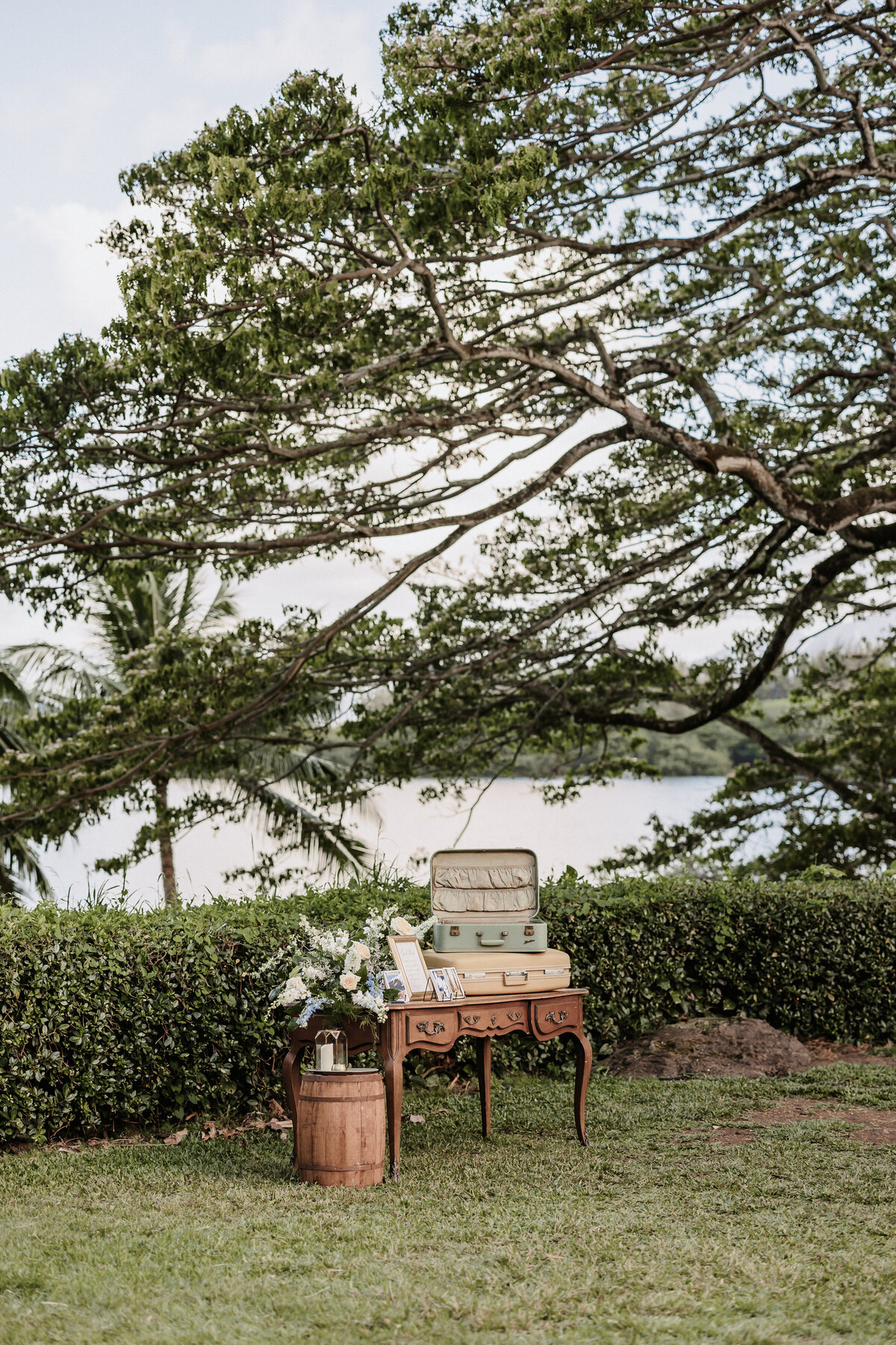 Wedding welcome trunk sititng on antique table surrounded by greenery and shrubs