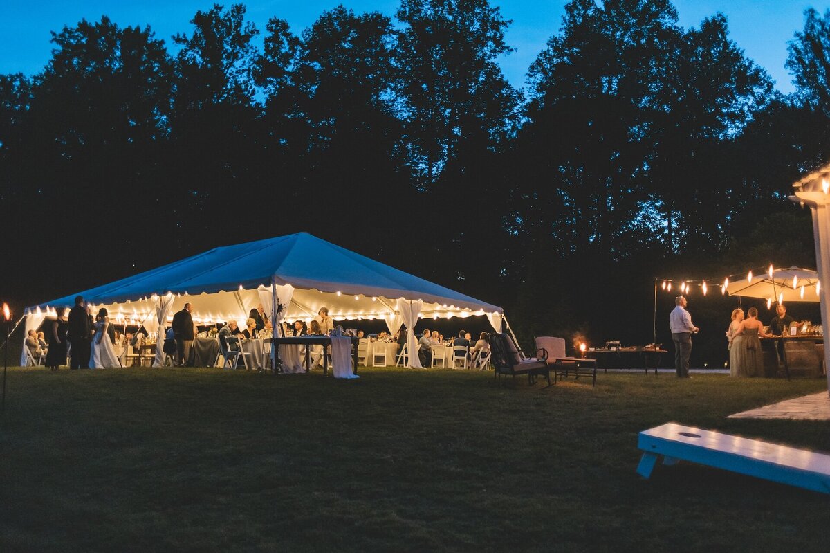 a white tent decorated with lights for a nighttime wedding reception