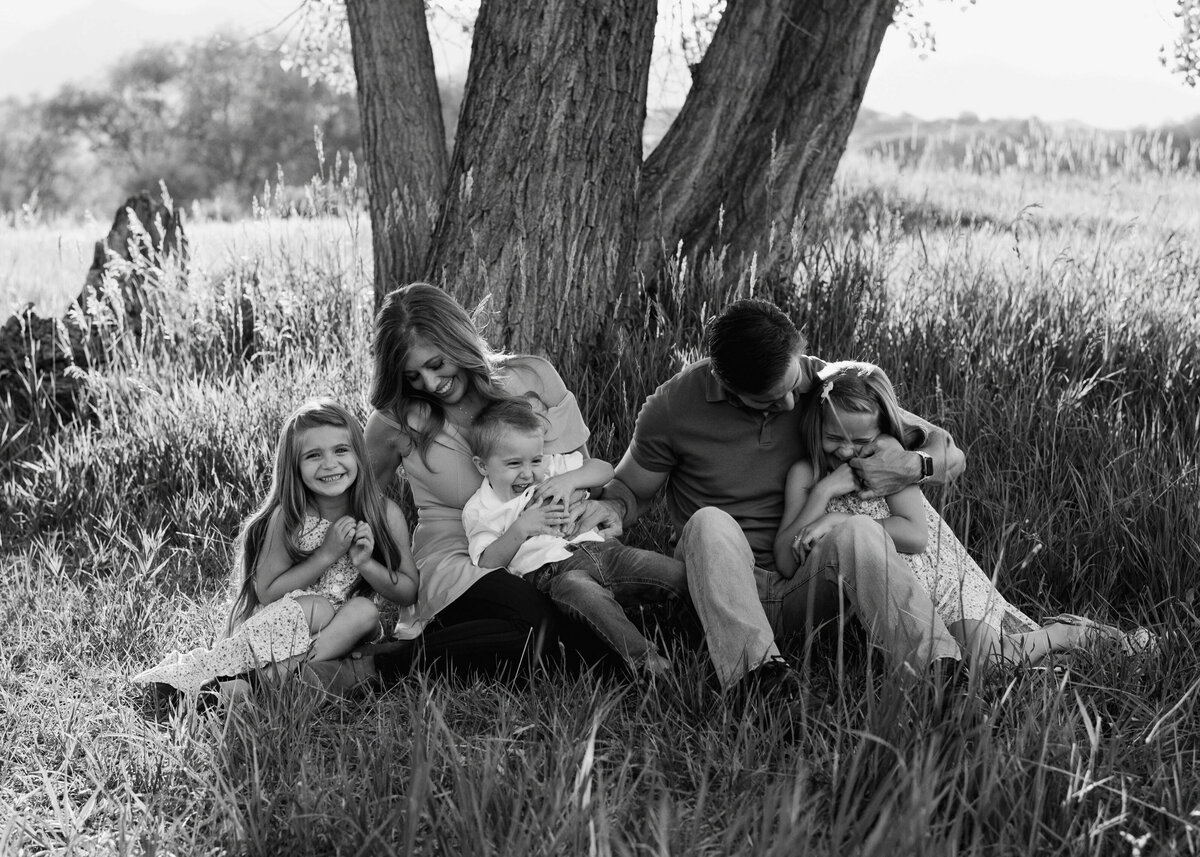 Shown in black and white, a family of five sit, tickle, and play with each other