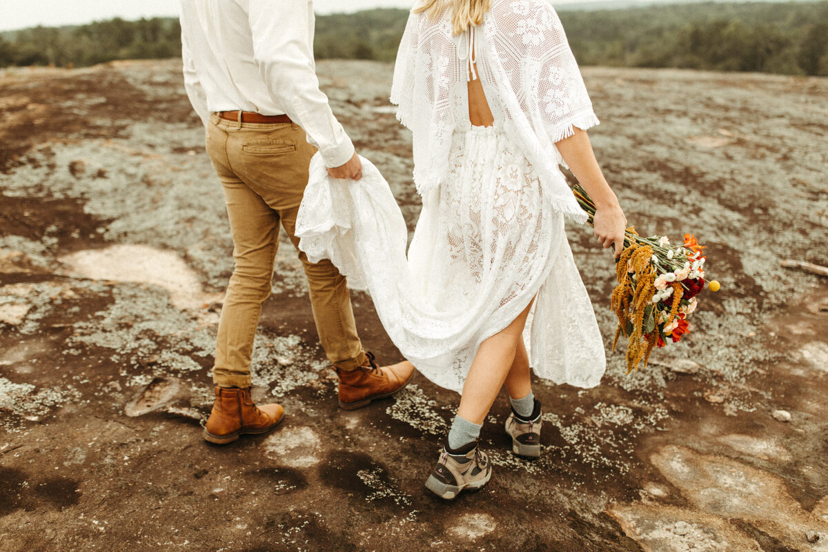 Groom carrying bride's boho wedding dress and showing their boots during their hiking elopement