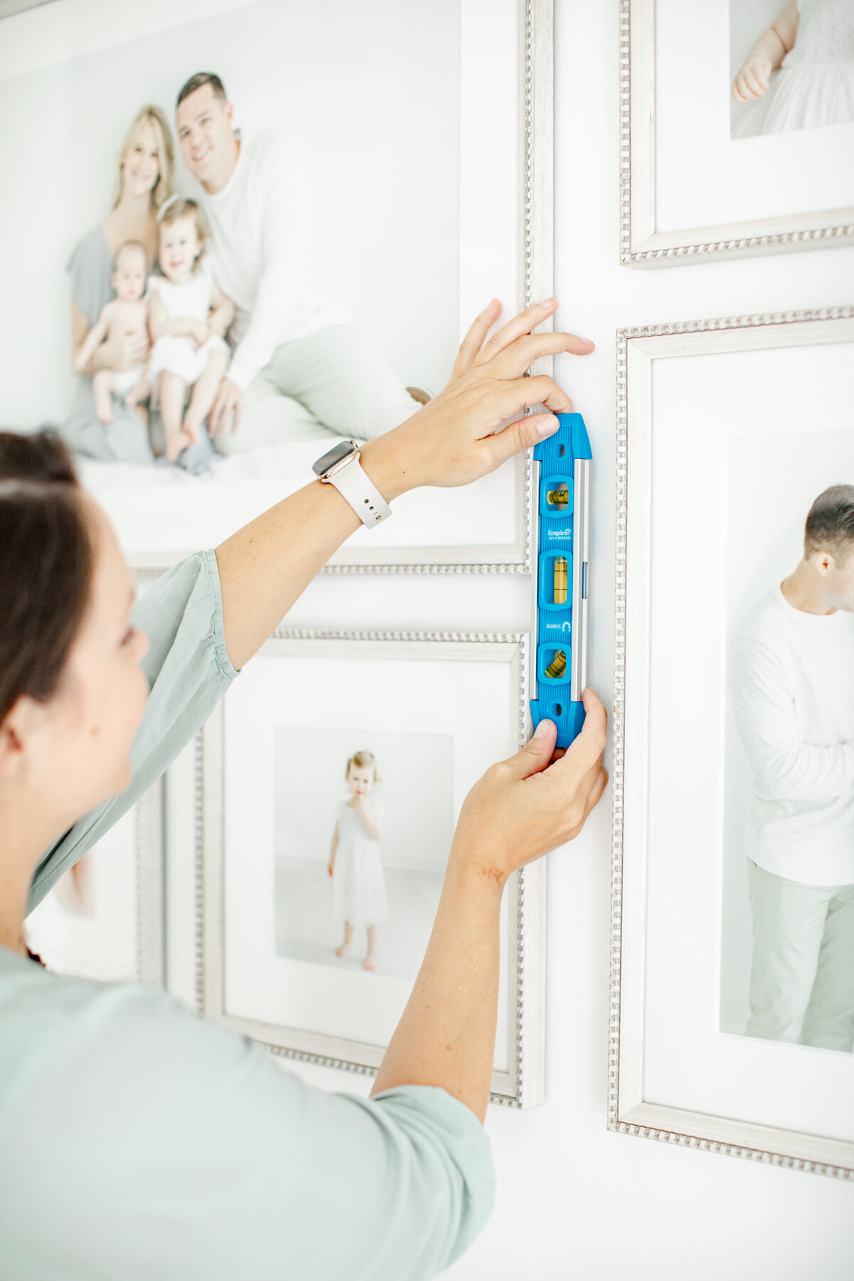 Woman levels framed family portraits in a home gallery wall