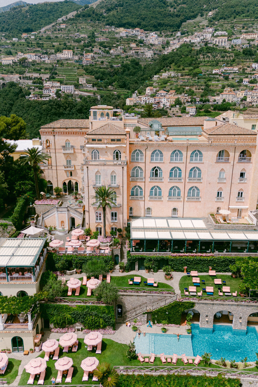 Aerial view of Palazzo Avino in Ravello, a luxury wedding venue on the Amalfi Coast with gardens, pool, and pink umbrellas.