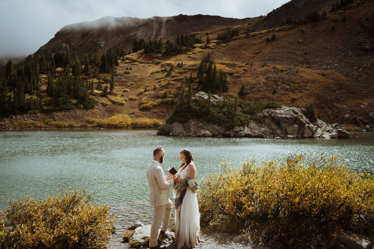 bride and groom standing in front of lake