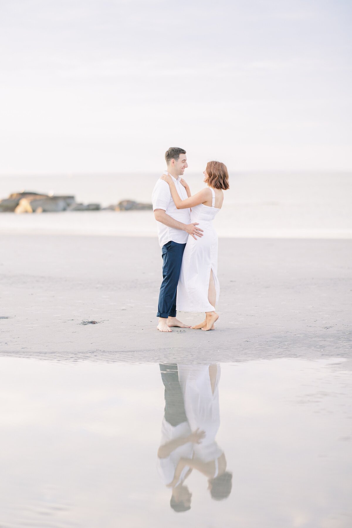A couple dancing on Wingaersheek Beach with a puddle in the foreground representing a Cape Cod engagement photographer's portfolio.
