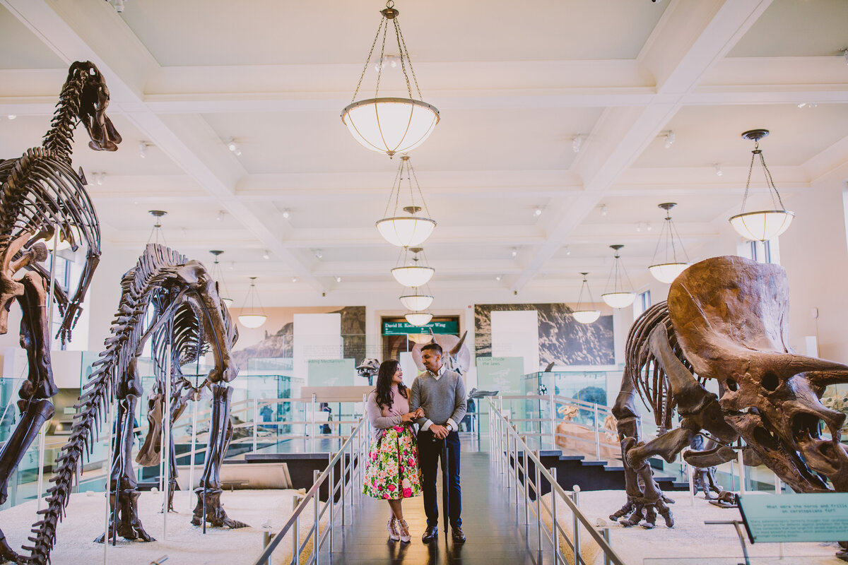 A couple standing inside the dinosaur exhibit at the museum of natural history in nyc during their engagement session