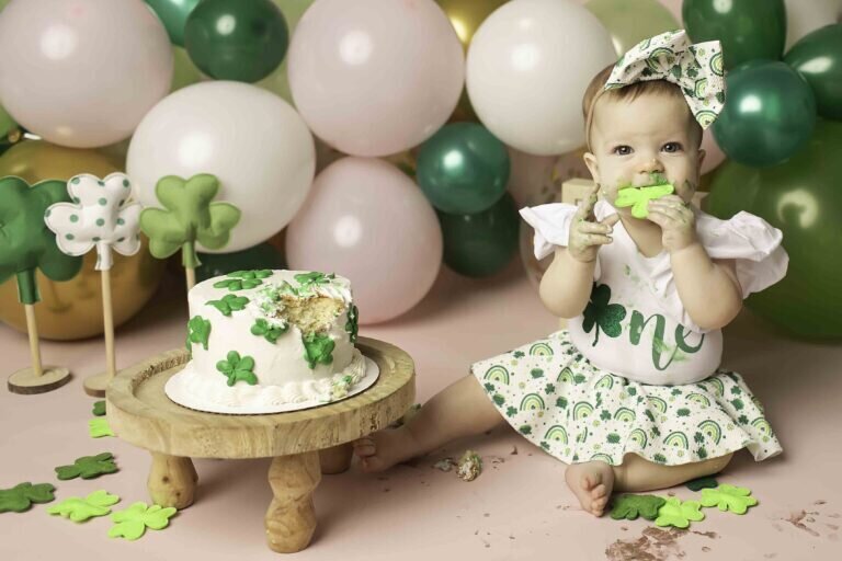 First birthday photoshoot with a baby sitting in front of a cake, looking at it curiously with a big smile