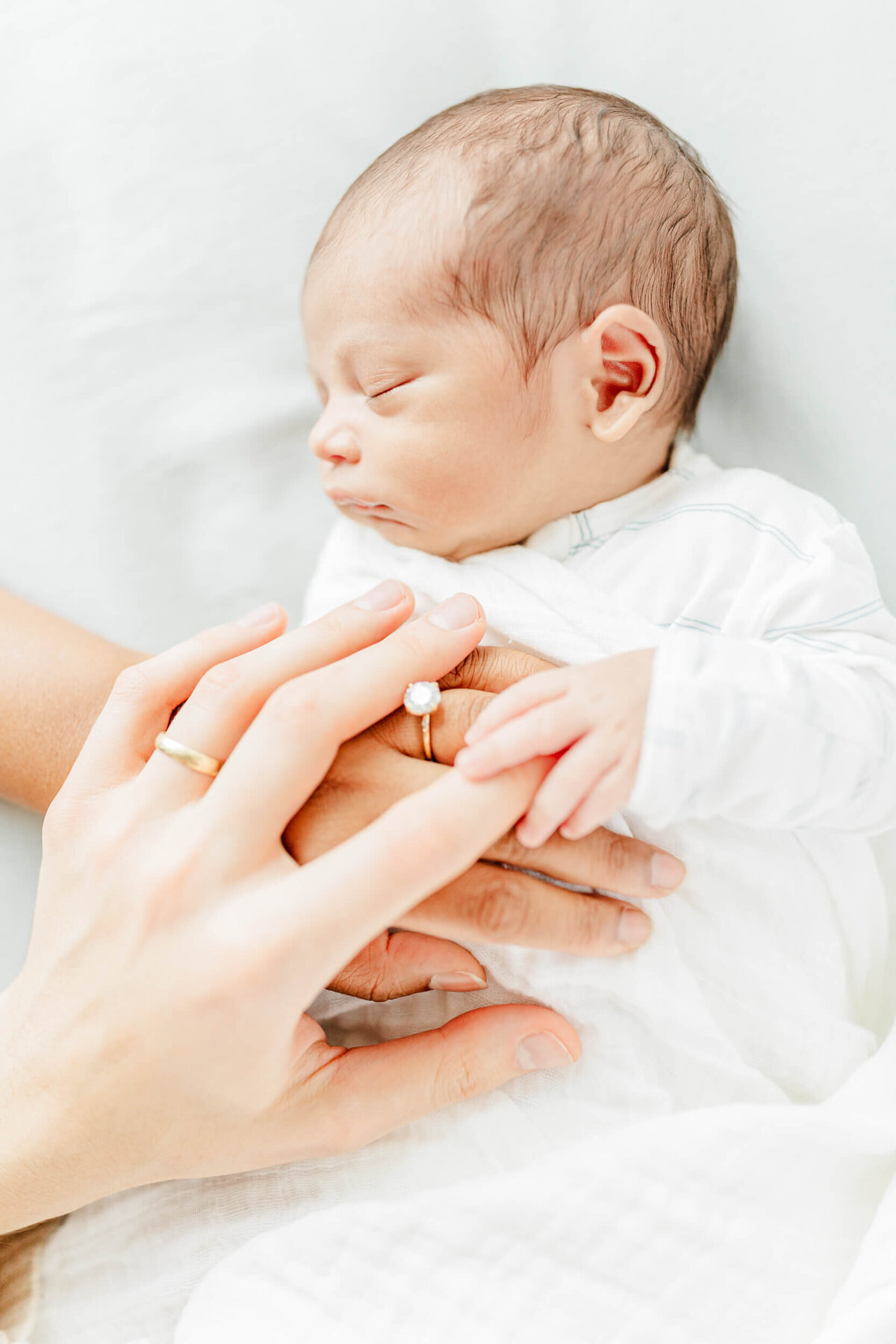 Mom and Dad's left hands rest on their newborn baby with their wedding rings visible