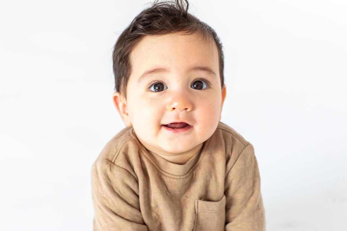 Studio-style portrait of a young toddler boy with big brown eyes, gazing directly at the camera with a curious and gentle expression