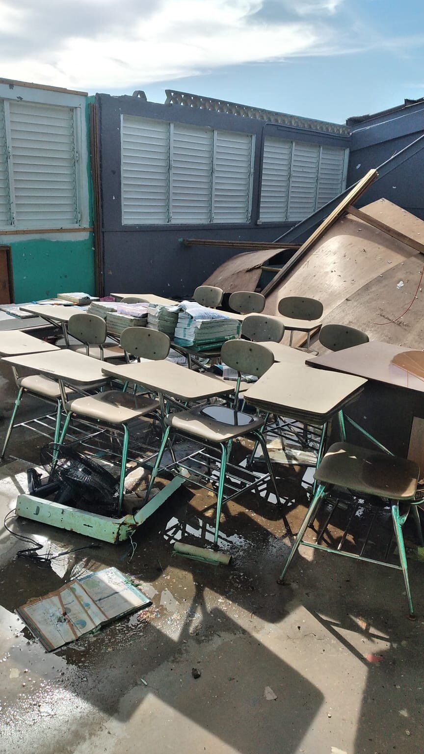 Destroyed classroom desks and scattered school supplies after hurricane flooding.