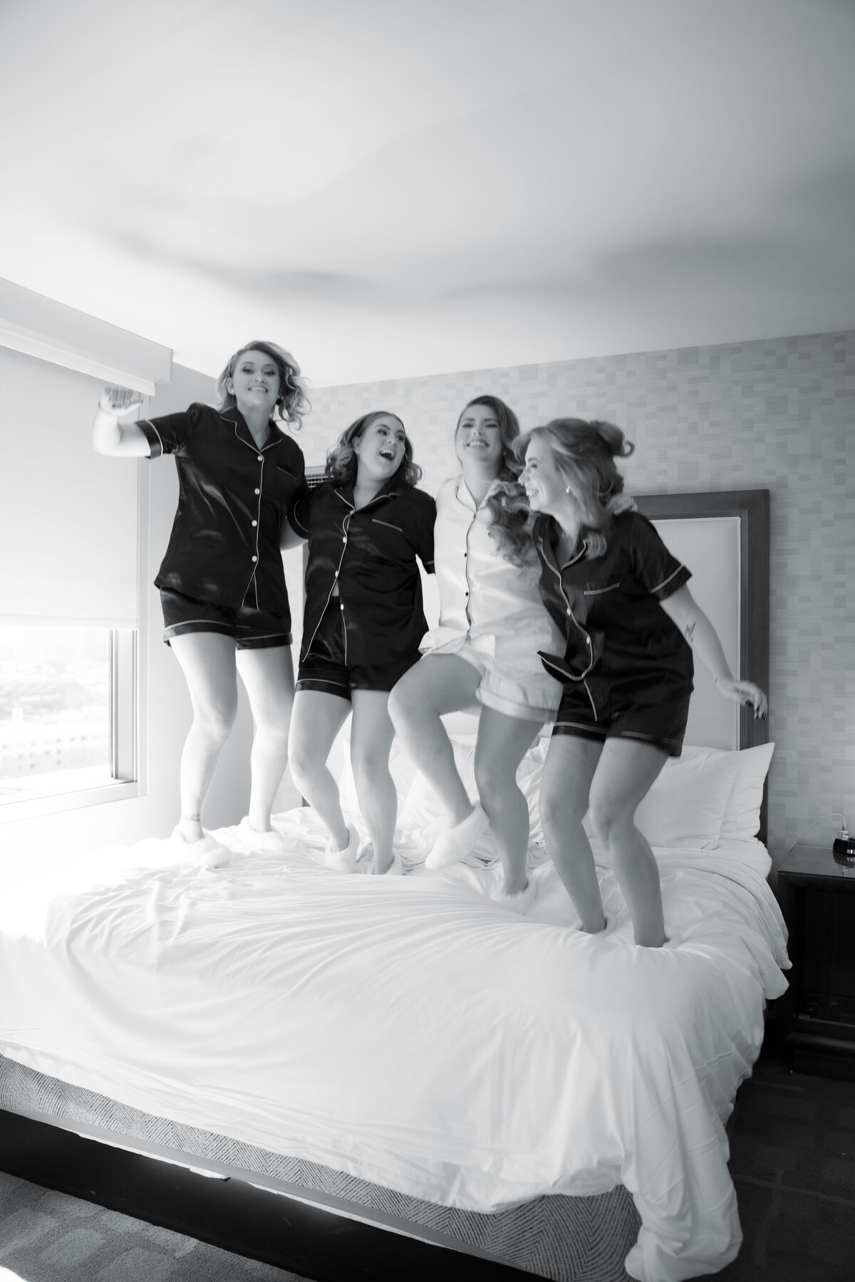Bride surrounded by her bridesmaids as they help her get ready for the wedding, sharing laughs and joyful moments in a softly lit room.