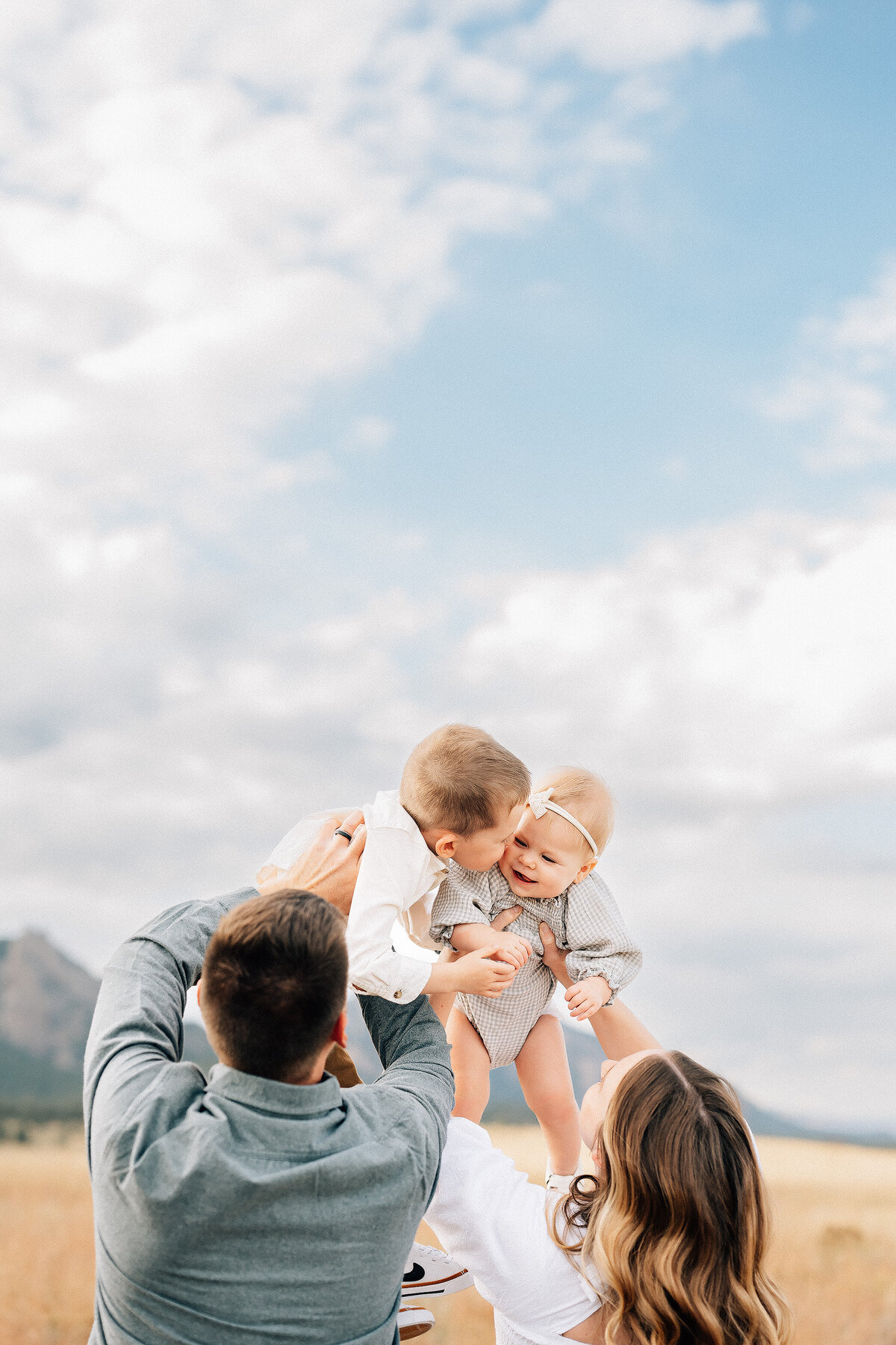 mom and dad lifting two children up to the sky with a large view of the clouds in the sky