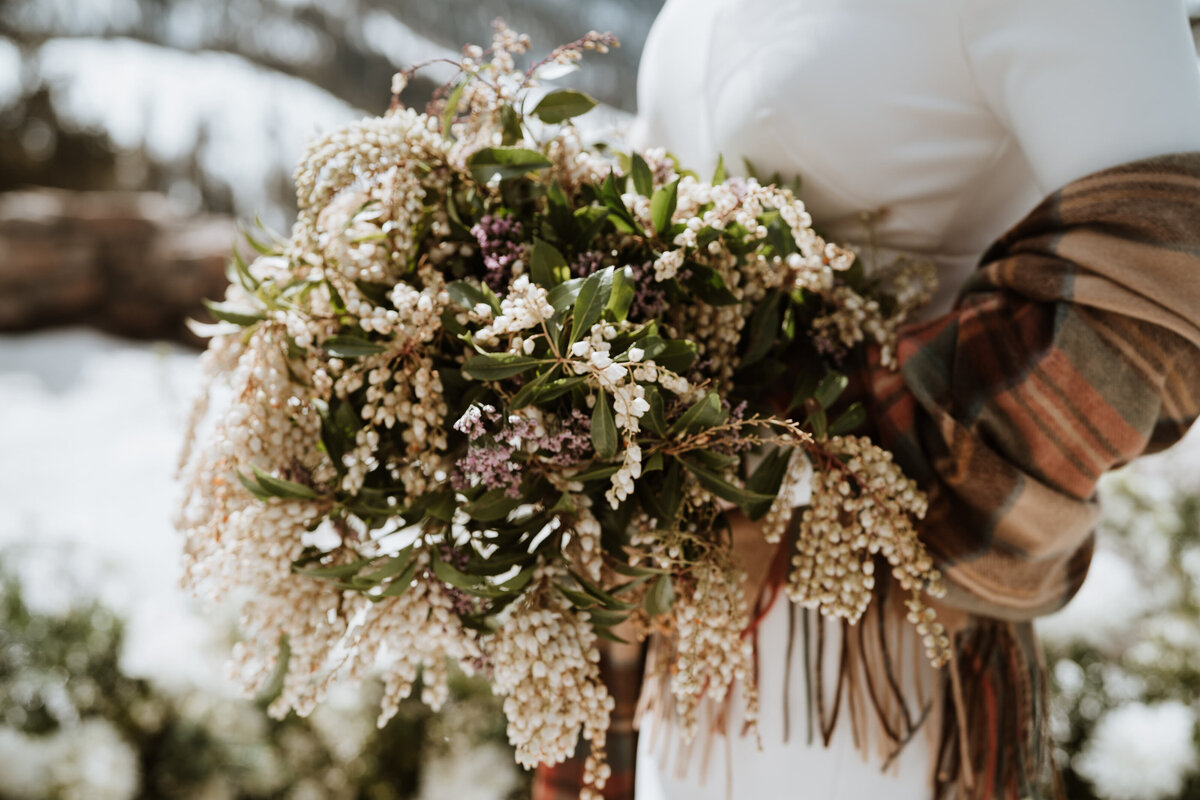 Close-up of winter bridal bouquet with white and purple blooms and plaid shawl.