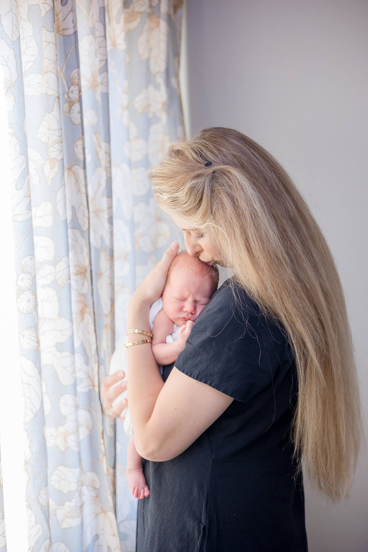 long blonde haired new mother kissing head of newborn son