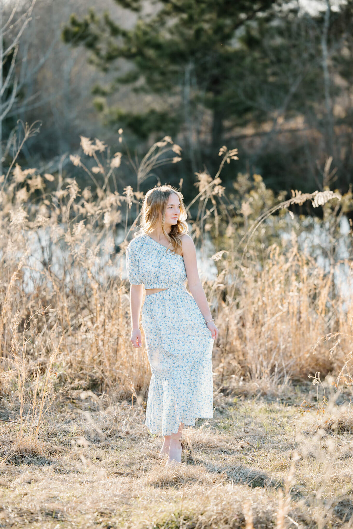 candid photograph of teenage girl wearing long dress while standing in open field during family photo session