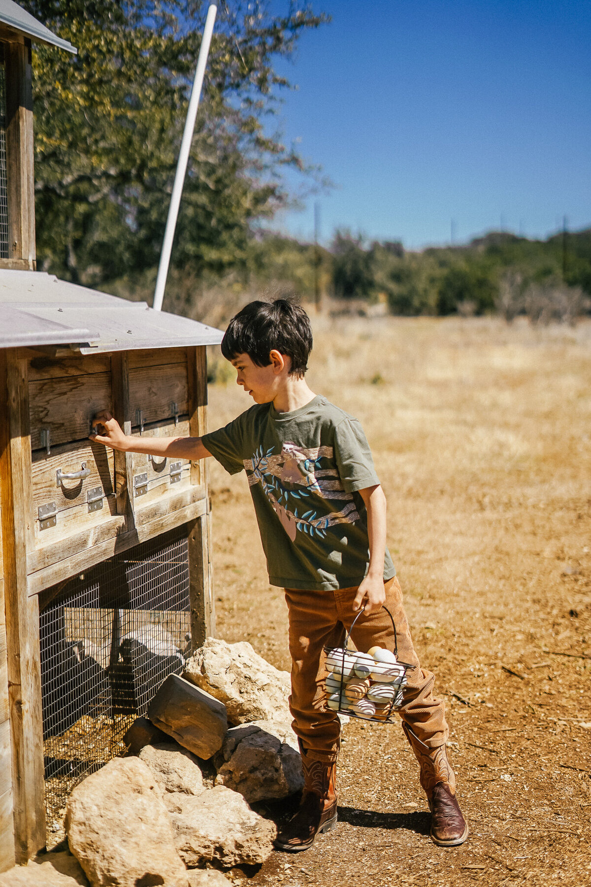 Young boy with a basket of eggs standing next to a chicken coop