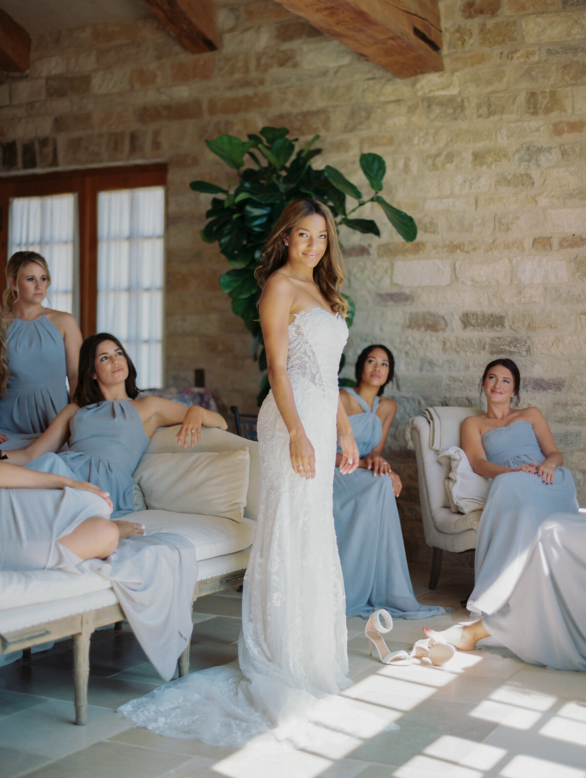 bride inside sunstone villa surrounded by bridemaids in light blue gowns sitting and smiling