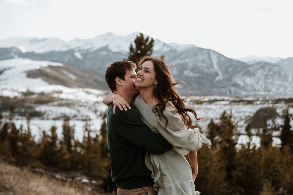 Groom-to-be lifts fiancée during joyful moment with snowy Breckenridge mountain backdrop.