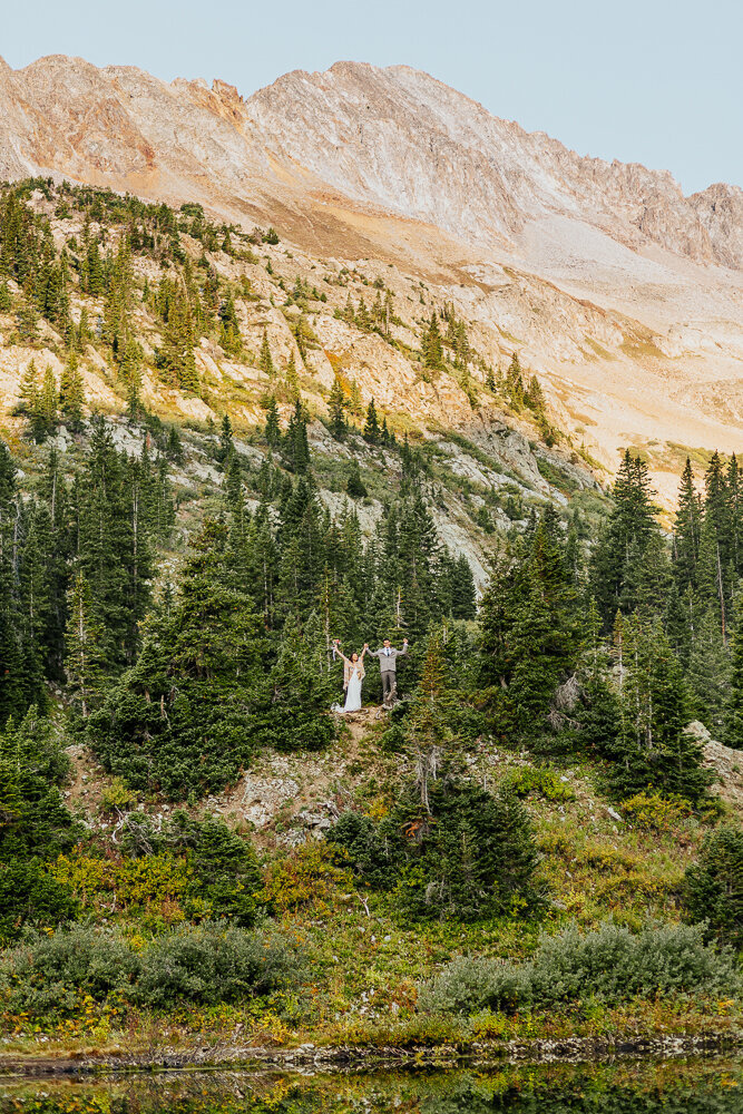 A couple celebrates on top of a mountain during their backpacking elopement in Crested Butte, Colorado.