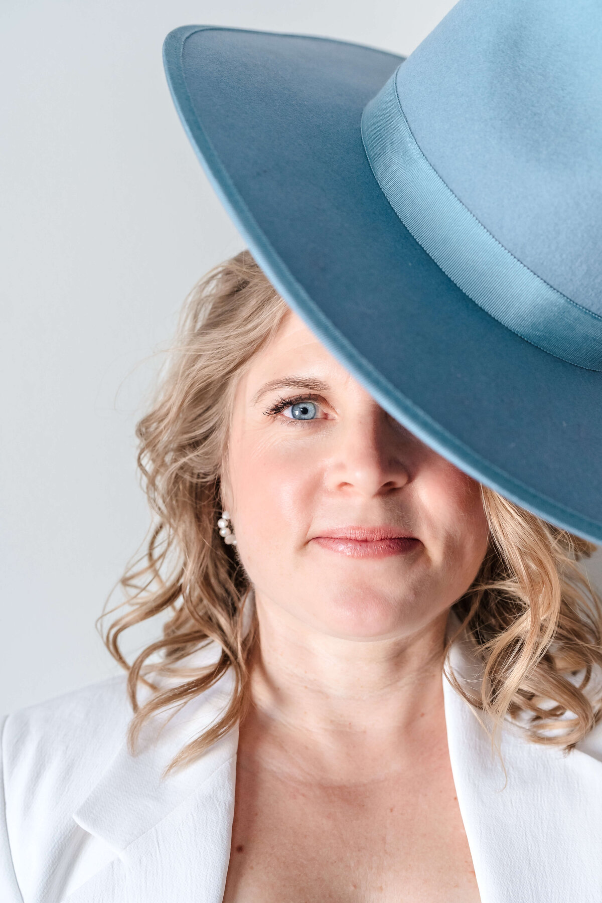 playful headshot of blonde woman partially hidden behind blue hat