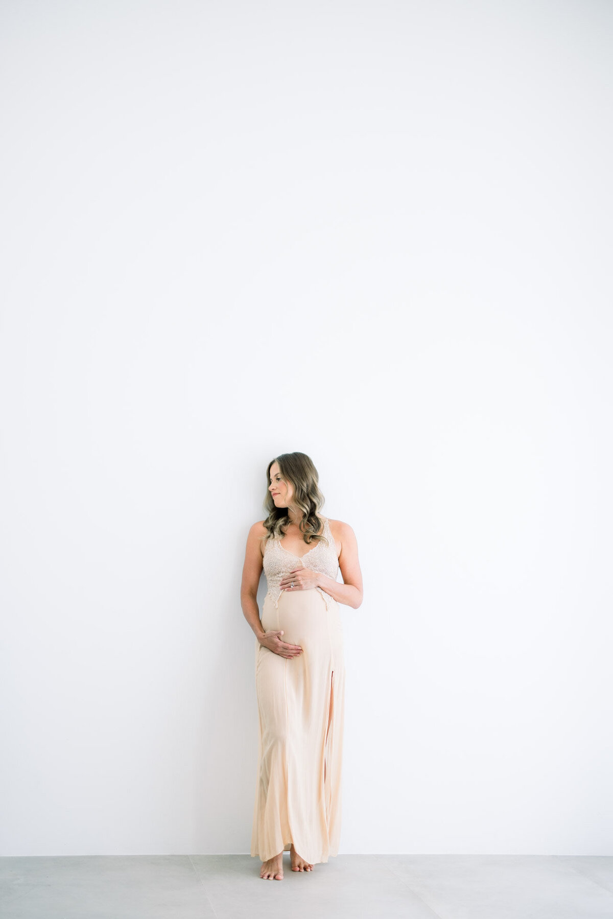 Pregnant woman leaning against wall holding belly Tampa maternity photographer Tina Marie Studio.