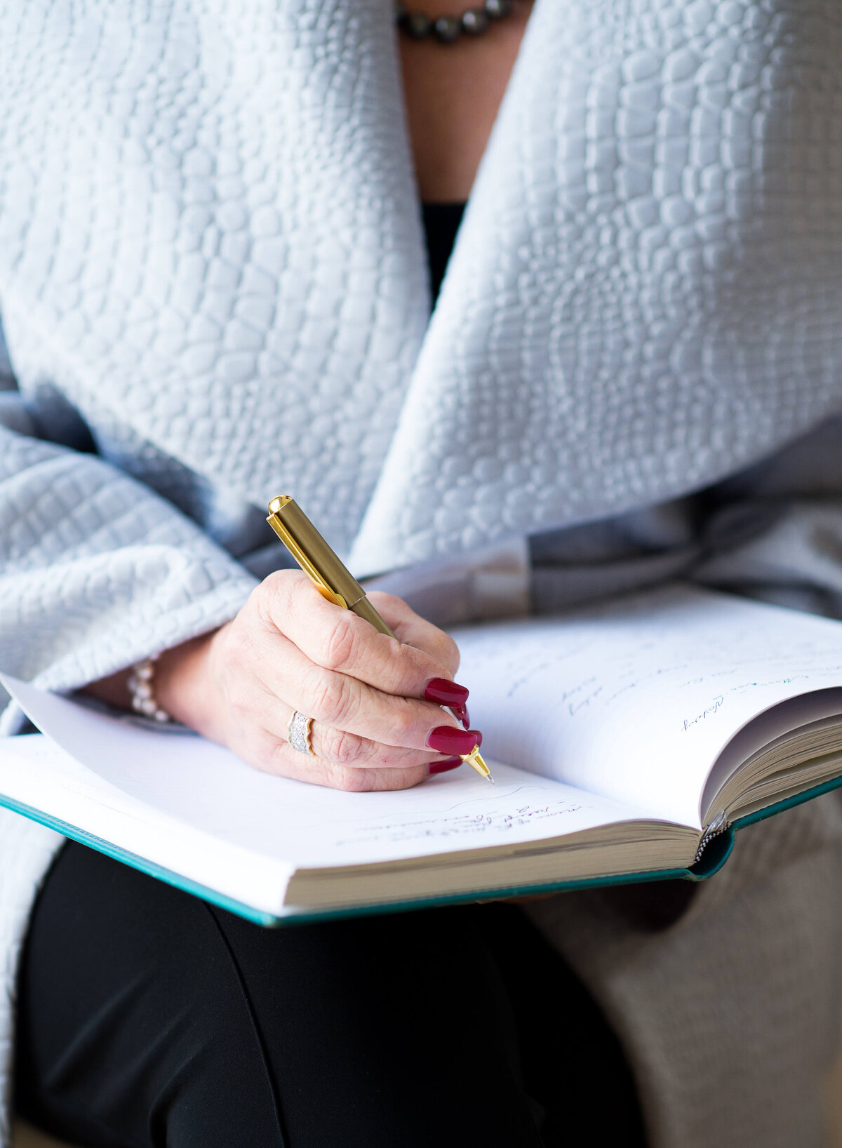 an action photo of a female realtor in a light blue jacket sitting in a chair writing in a day-planner.  Taken indoors by Ottawa Branding Photographer JEMMAN Photography COMMERCIAL