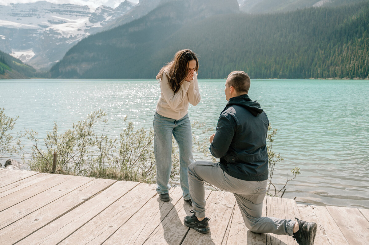 Proposal on wooden deck at Lake Louise with woman surprised and emotional.